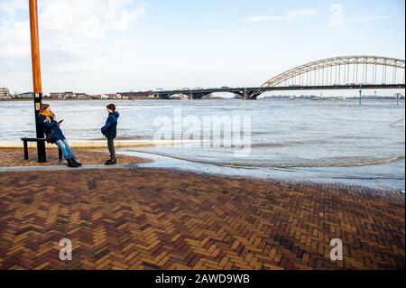 Nijmegen, Gelderland, Niederlande. Februar 2020. Eine Frau, die mit ihrem Sohn näher an der Hochwasserzone spricht.Überschwemmungsgebiete am Rheinufer und andere größere Flüsse werden voraussichtlich später am Wochenende unter Wasser sein. Nijmegen ist eine der niederländischen Städte, die jetzt von diesem hohen Wasserstand betroffen sind. Die Waalkade, die Zone näher am Fluss, wurde für den Verkehr gesperrt und es wird erwartet, dass das Wasser eine Höhe von mehr als 11 Metern über dem Meeresspiegel erreichen kann. Das Rheinwasser bei Lobith, wo der Fluss in die Niederlande übergeht, soll rund 14 Meter erreichen Stockfoto