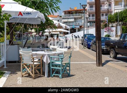 Neos Marmaras, Chalkidiki, Griechenland. 16. Juni 2019: Gemütliche Straße der Küstenstadt in Griechenland. Straßencafé mit ruhenden Menschen, geparkten Autos, Häusern mit Spa Stockfoto