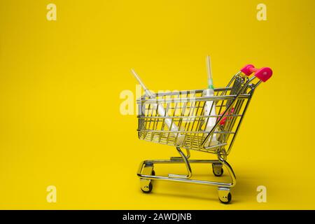 Konzept der medikamentösen Behandlung. Nehmen Sie die vom Arzt verordnete Behandlung. Der Korb des Verbrauchers auf gelbem Hintergrund mit vielen Medikamenten. Ampullen mit Impfstoff Stockfoto