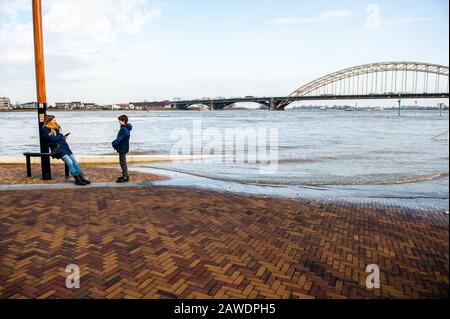 Nijmegen, Gelderland, Niederlande. Februar 2020. Eine Frau, die mit ihrem Sohn näher an der Hochwasserzone spricht.Überschwemmungsgebiete am Rheinufer und andere größere Flüsse werden voraussichtlich später am Wochenende unter Wasser sein. Nijmegen ist eine der niederländischen Städte, die jetzt von diesem hohen Wasserstand betroffen sind. Die Waalkade, die Zone näher am Fluss, wurde für den Verkehr gesperrt und es wird erwartet, dass das Wasser eine Höhe von mehr als 11 Metern über dem Meeresspiegel erreichen kann. Das Rheinwasser bei Lobith, wo der Fluss in die Niederlande übergeht, soll rund 14 Meter erreichen Stockfoto