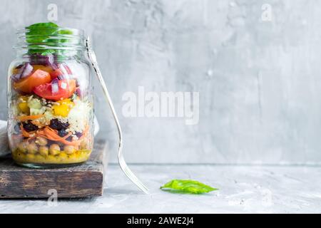 Köstlicher frischer vegetarischer bunter Salat in den Gläsern mit Kichererbsen, Paprika, Gurke, Karotte, getrockneten Preiselbeeren, Tomaten, roter Zwiebel und Kürbisse Stockfoto