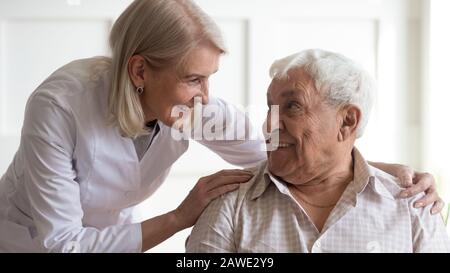 Positive weibliche Krankenschwester, die sich um eine ältere männliche Patientin kümmert Stockfoto