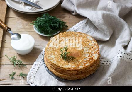 Buchweizenpfannkuchen serviert mit saurer Sahne und Dill auf einem Holztisch. Rustikaler Stil. Stockfoto