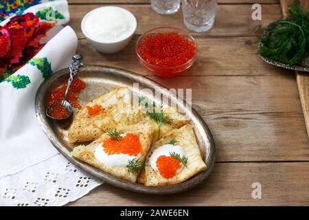 Hausgemachte Pfannkuchen mit rotem Kaviar, saurer Sahne und Dill serviert mit Wodka. Rustikaler Stil. Stockfoto