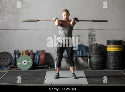 Junge Frau, die sich aufwärmt und sich auf das schwere Heben im Fitnessstudio vorbereitet. Stockfoto