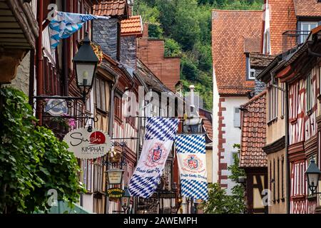 Miltenberg, DEUTSCH - 07.07.2019: Fahnen und Schilder außerhalb der hübschen mittelalterlichen Fachwerkbauten in der Hauptstraße in der Altstadt Stockfoto