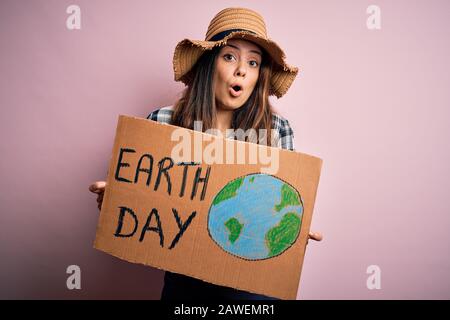 Junge, schöne Frau, die nach einer Konservierung des Planeten fragt, die Pappe hält, die den Erdtag feiert, die mit einem Überraschungsgesicht erschreckt wurde, Angst und Erregung Stockfoto