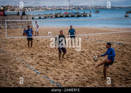 Männer, die footvolley am Strand Praia da Ribeira, dem Hauptstrand von Cascais, spielen, der zum zentralen Platz der Stadt blickt und den Fischerhafen überblickt Stockfoto