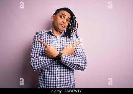 Junger, gutaussehender afro-amerikanischer afro-Mann mit Dreadlocks, der ein leeres Hemd Trägt, Das Mit den Fingern auf beide Seiten zeigt, andere Richtungen sind anderer Meinung Stockfoto