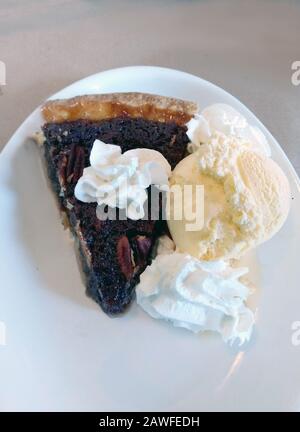 Ein heißes Stück Schokoladenpecan Pie ist frisch aus dem Ofen und wird mit einer Schaufel Vanilleeisscreme und ein paar Puppen Schlagsahne serviert Stockfoto