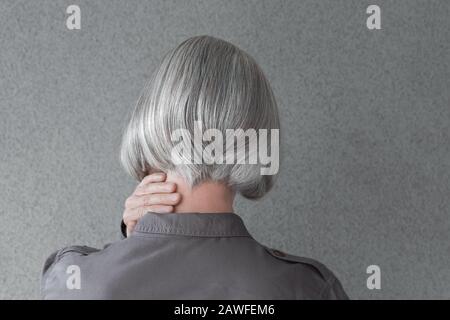 Frau mit silbergrauem Haar, die Hand an ihrem Hals hält, von hinten. Stockfoto