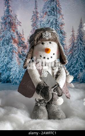 Ein wunderbarer, gefüllter Schneemann steht vor einem verschneiten Winterhintergrund und überhäuft einen Holzschlitten Stockfoto