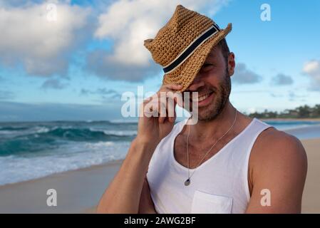 Junges kaukasisches Männchen, das am Sunset Beach auf Hawaii steht und einen Strohhut mit dem Ozean im Hintergrund trägt Stockfoto