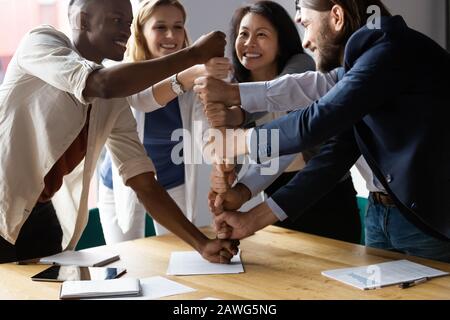 Zufriedene Mitarbeiter, die auf Unternehmensmeeting Fäuste stapeln und Erfolg feiern Stockfoto