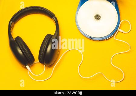 Schwarze Kopfhörer mit weißem Kabel auf gelbem Hintergrund. CD-Player mit weißer cd und Ohrhörer Stockfoto