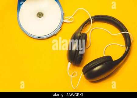 Schwarze Kopfhörer mit weißem Kabel auf gelbem Hintergrund. CD-Player mit weißer cd und Ohrhörer Stockfoto