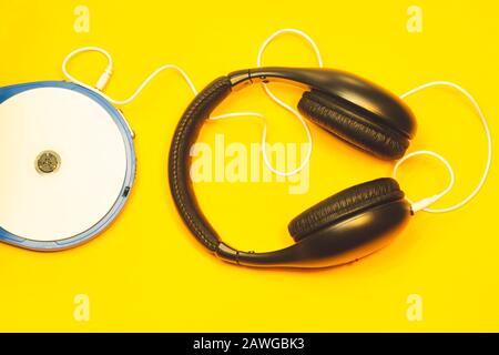 Schwarze Kopfhörer mit weißem Kabel auf gelbem Hintergrund. CD-Player mit weißer cd und Ohrhörer Stockfoto