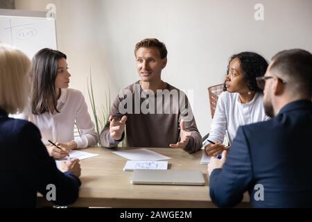 Verschiedene Geschäftsleute hören dem Teamleiter zu, der am Tisch im Büro sitzt Stockfoto