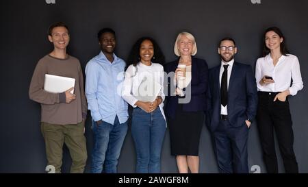 Eine Gruppe von Mitarbeitern aus mehreren ethnischen Gruppen, die in Innenräumen lächelnde Geräte halten Stockfoto