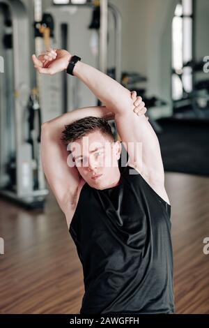 Gutaussehender junger Mann, der beim Aufwärmen die Arme und Rücken streckt, bevor er im Fitnessstudio trainiert Stockfoto