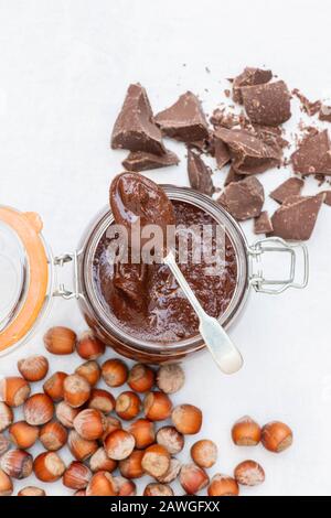 Hausgemachte vegane Haselnussschokolade in einem kilner Glas mit ungeschälten Haselnüssen und Brocken dunkler Schokolade Stockfoto