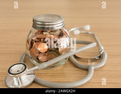 Coin jar, Stethoskop auf dem Schreibtisch. Konzept der Altersvorsorge, persönliche Finanzplanung, Krankenversicherung. Stockfoto