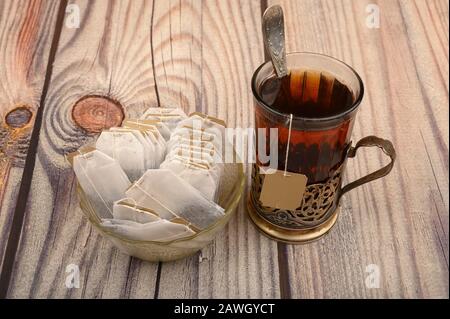 Tee aus facettiertem Glas in einem Vintage-Cup-Halter und Teebeutel in einer Glasvase auf Holzhintergrund. Nahaufnahme Stockfoto