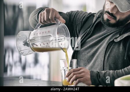 Gesundes Ernährungskonzept des jungen starken Mannes mit Bart-füllendem Glas mit gelbem Orangensaft nach hartem Training im Sportstudio Stockfoto