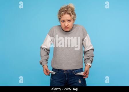 Kein Bargeld. Verärgerte arme Frau mit kurzen lockigen Haaren in legeren Sweatshirts, die leere Taschen herausdrehen, kein Geld für das Leben, die Schulden und den Bankrott haben Stockfoto