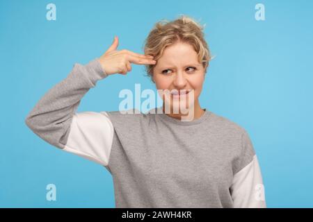 Tötet mich bitte. Depressive Frau mit geschweiften Haaren im Sweatshirt, die mit der Fingerpistole auf den Kopf zeigt und erschrocken aussieht, an Selbstmord denkt und die Handpistole anvisiert Stockfoto