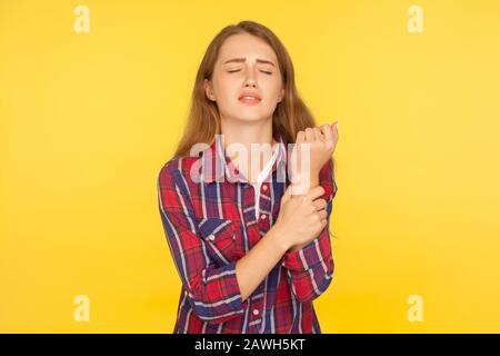 Porträt des ungesunden Ingwermädchens im karierten Hemd, das mit schmerzhaften Schmerzen steht und das Wunde Handgelenk berührt, Handschädigungen, Verstauchung, Gelenkentzündung. In Stockfoto