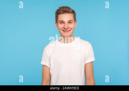 Porträt eines gutaussehenden fröhlichen, freundlichen Kerls im zwanglosen weißen T-Shirt im stehen, lächelnd vor der Kamera mit gutmütigem, liebenswürdigen, liebenswürdigen Ausdruck, optimistischer Stimmung Stockfoto