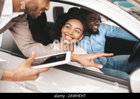 Glückliches Paar Kauft Auto Im Gespräch Mit Einem Verkäufer, Der In Auto Sitzt Stockfoto