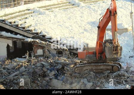 Ein Bagger arbeitet an einer Baustelle, die Bauschutt im Winter in Russland auf Schneegrund lädt. Stockfoto