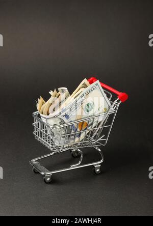 Ein Miniatur-Einkaufswagen mit US-Dollar-Banknoten vor dunklem Hintergrund. Stockfoto