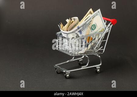 Ein Miniatur-Supermarkt-Einkaufswagen mit US-Dollar-Banknoten auf dunklem Hintergrund. Stockfoto