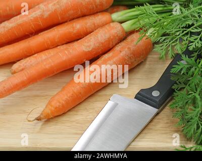 Frische Karotten mit Messer auf einem Holzschneidebrett, Nahaufnahme Stockfoto