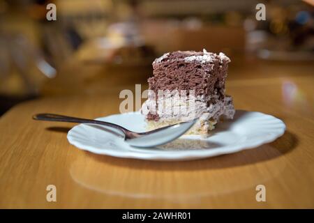 Weißer, gehackter Background aus Kuchenteig in einem weißen Teller. Löffel. Brauner und weißer Kuchen auf Holzbrett . Kuchen mit Keks und Sahne. Aus Holz Stockfoto