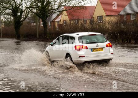 Ein Auto, das in Kirkham, Lancashire, Großbritannien, mit hoher Geschwindigkeit durch tiefes Hochwasser fährt und dabei auf einer Straße Spray aufsprüht. Februar 2020. Wetter in Großbritannien; Sturm Ciara Straßen überflutet in Kirkham. Quelle: MediaWorldImages/Alamy Live News Stockfoto