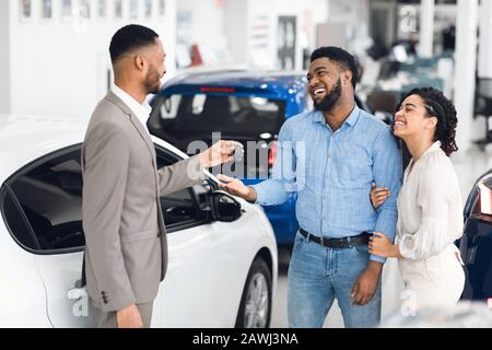 Paare, Die Ein Auto Kaufen Und Den Schlüssel Vom Verkäufer Im Auto-Showroom Holen Stockfoto