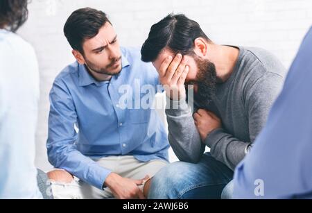 Gruppenmitglieder trösten weinenden süchtigen Mann bei Reha-Sitzung Stockfoto