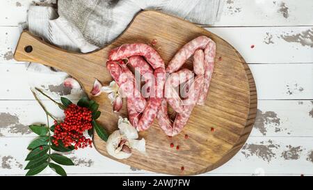 Die spanische Longaniza es un embutido largo originario de España, rohe Rinderwürste, die mit pinkfarbenem Pfeffer auf dem Schneidebrett hausgemacht wurden Stockfoto