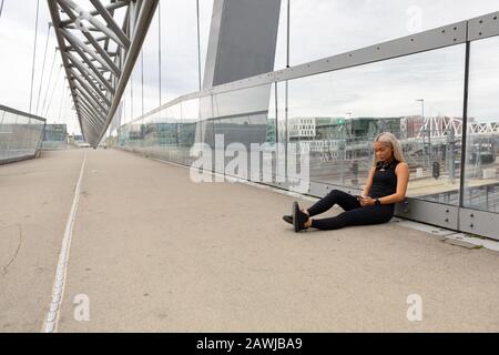Läufer, Der Nach Dem Training Auf Bridge Ruht und die Wokout-Leistung überprüfen Stockfoto