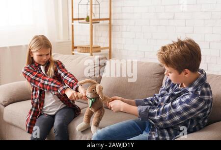 Gieriger Bruder Und Schwester Ziehen Apart Toy Auf Sofa Sitzen Stockfoto