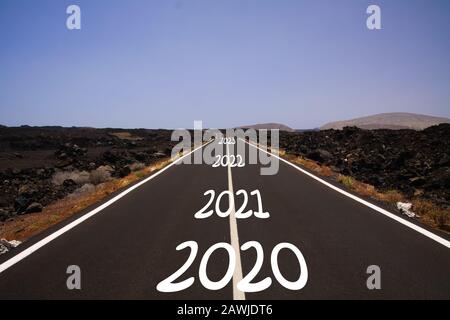 Langes hartes Erfolgskonzept: Blick auf endlose Asphaltstraße durch trockene, aride Vulkanlandschaft mit den Jahren 2020, 2021, 2022, 2023 Stockfoto