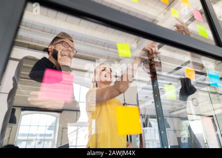 Geschäftsleute treffen sich im Büro und verwenden Post-it-Notizen, um Ideen auszutauschen. Brainstorming-Konzept. Haftnotiz an der Glaswand. Stockfoto