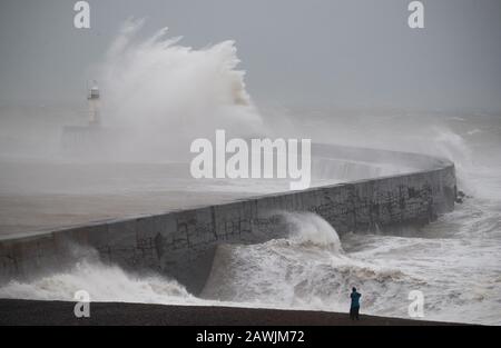 Die Menschen blicken auf das Meer, während Wellen in Newhaven in East Sussex in das Wellenbrecher stürzen. Stockfoto