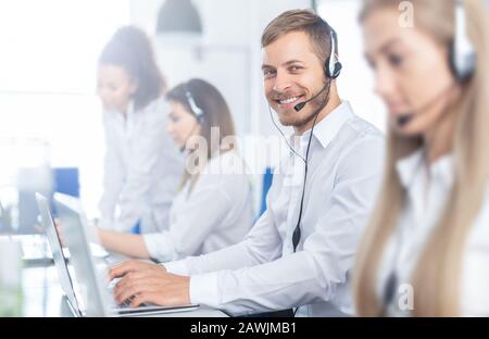 Call Center Arbeitnehmer, der von seinem Team begleitet. Lächelnd customer support Operator bei der Arbeit. Junge Mitarbeiter mit einem Headset. Stockfoto