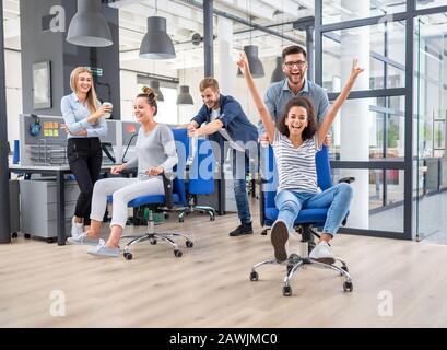 Junge freundliche Geschäft Leute in ungezwungener Kleidung Spaß am Rudern Stühle in einem modernen Büro. Happy Team Konzept. Stockfoto