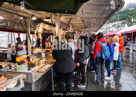 Redaktion 09.04.2019 Bergen Norwegen Touristen auf dem Fischmarkt kaufen Mittagessen an einem regnerischen Tag Stockfoto